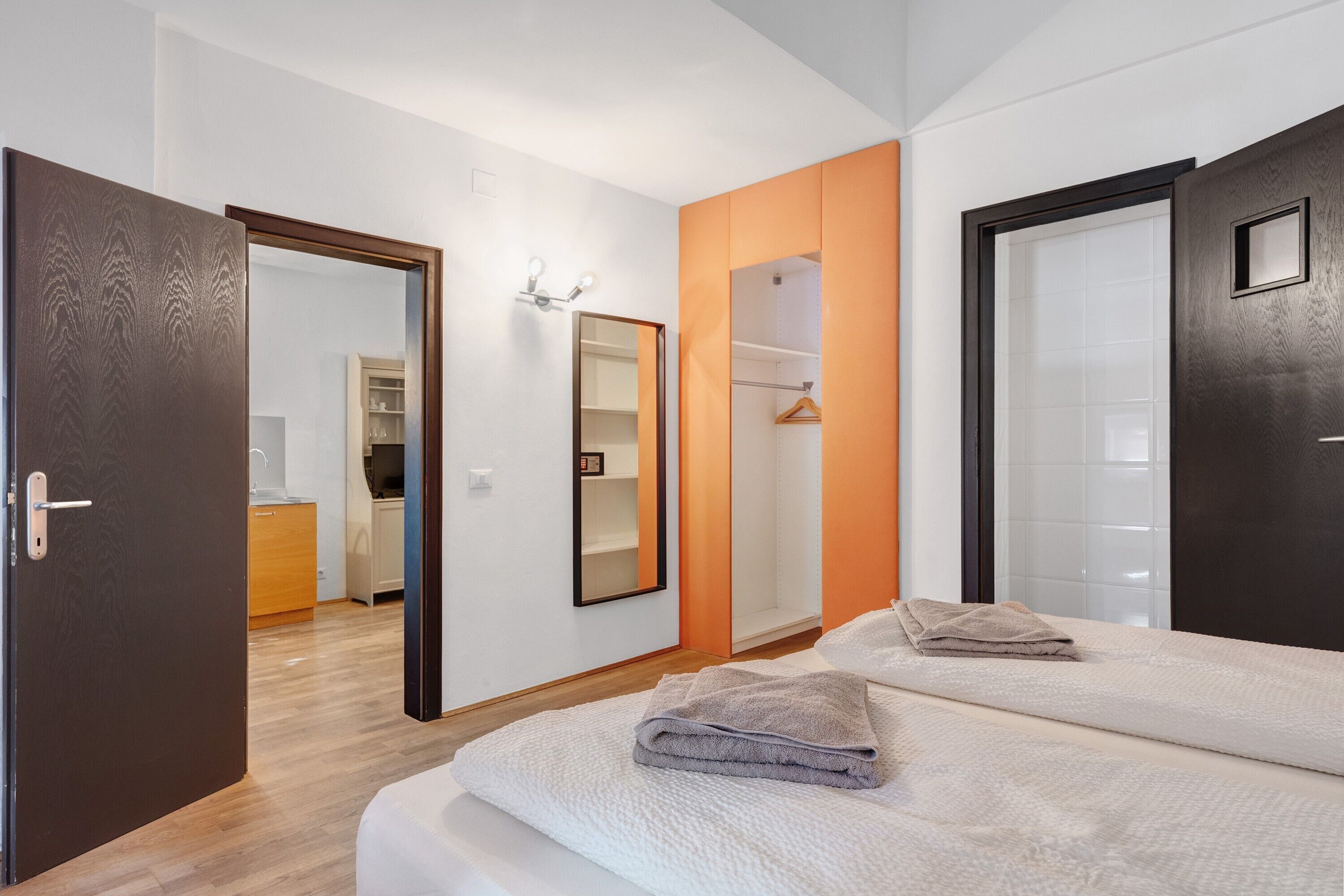 Ein modernes Schlafzimmer mit einem großen Bett, einem Kleiderschrank, einem Spiegel und einem durch eine offene Tür einsehbaren Badezimmer.