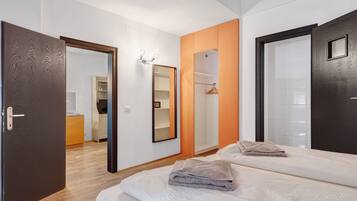 Une chambre moderne avec un grand lit, une armoire, un miroir et une salle de bain visible à travers une porte ouverte.