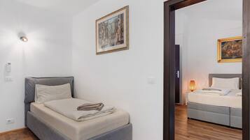 Um quarto com cama, mesa de cabeceira, luminária na parede e um quadro emoldurado.