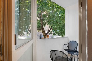 A balcony with a view of a tree and a building. There are two chairs on the balcony.