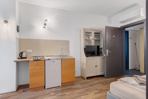 A compact kitchen with a sink, a small refrigerator, and a microwave. There's a cabinet with glass doors and a television on top.