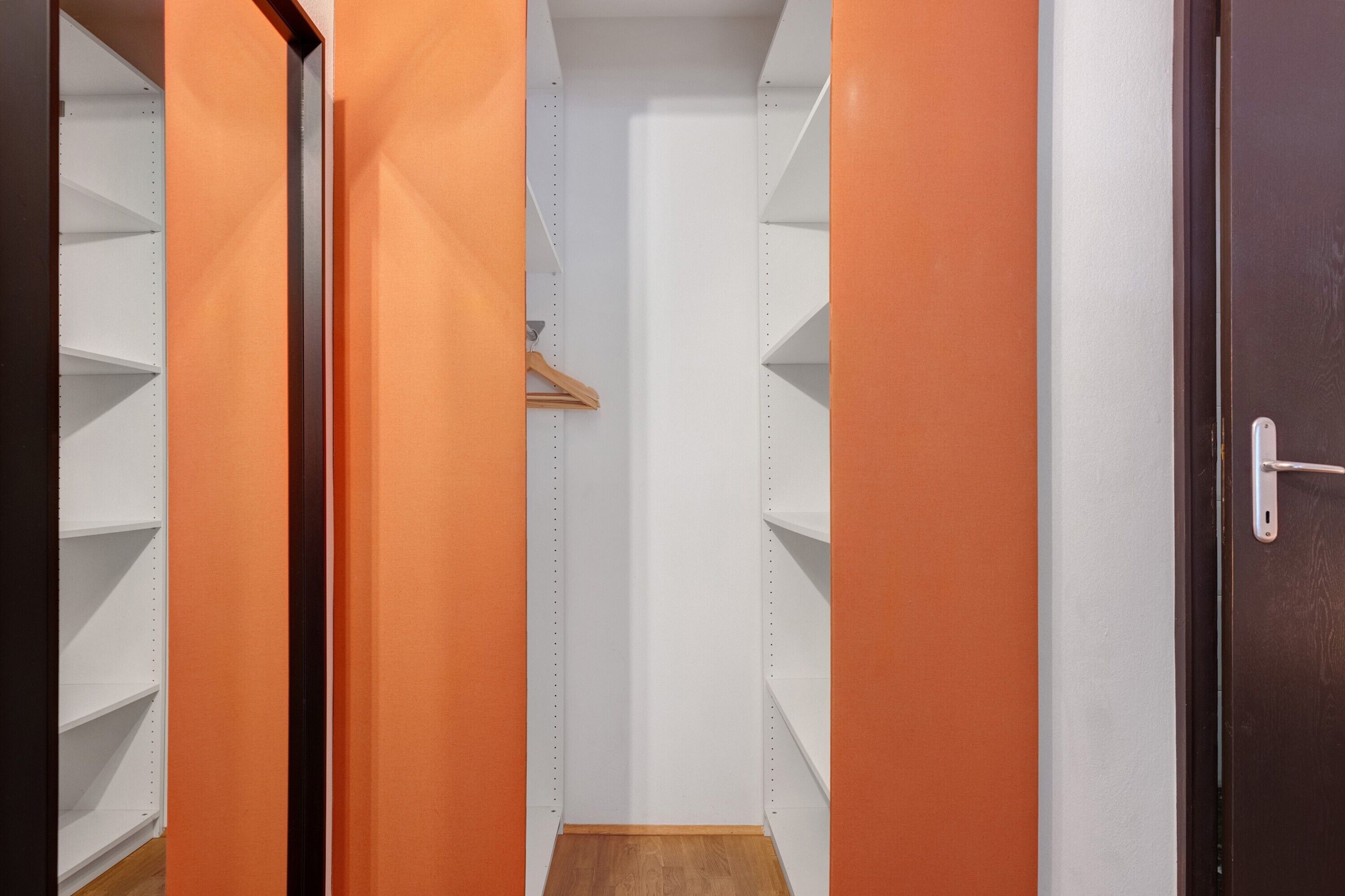A narrow hallway with orange walls and white shelving units.