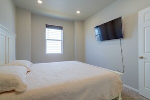 A bedroom with a bed, a window, a wall-mounted TV, and a door. - Private Yard w/ Patio! Modern Commerce City Gem (Commerce City)