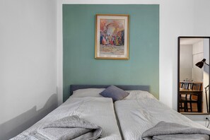 Ein Schlafzimmer mit einem Bett, einem Gemälde, einem Spiegel und einem Schreibtisch mit einer Lampe.