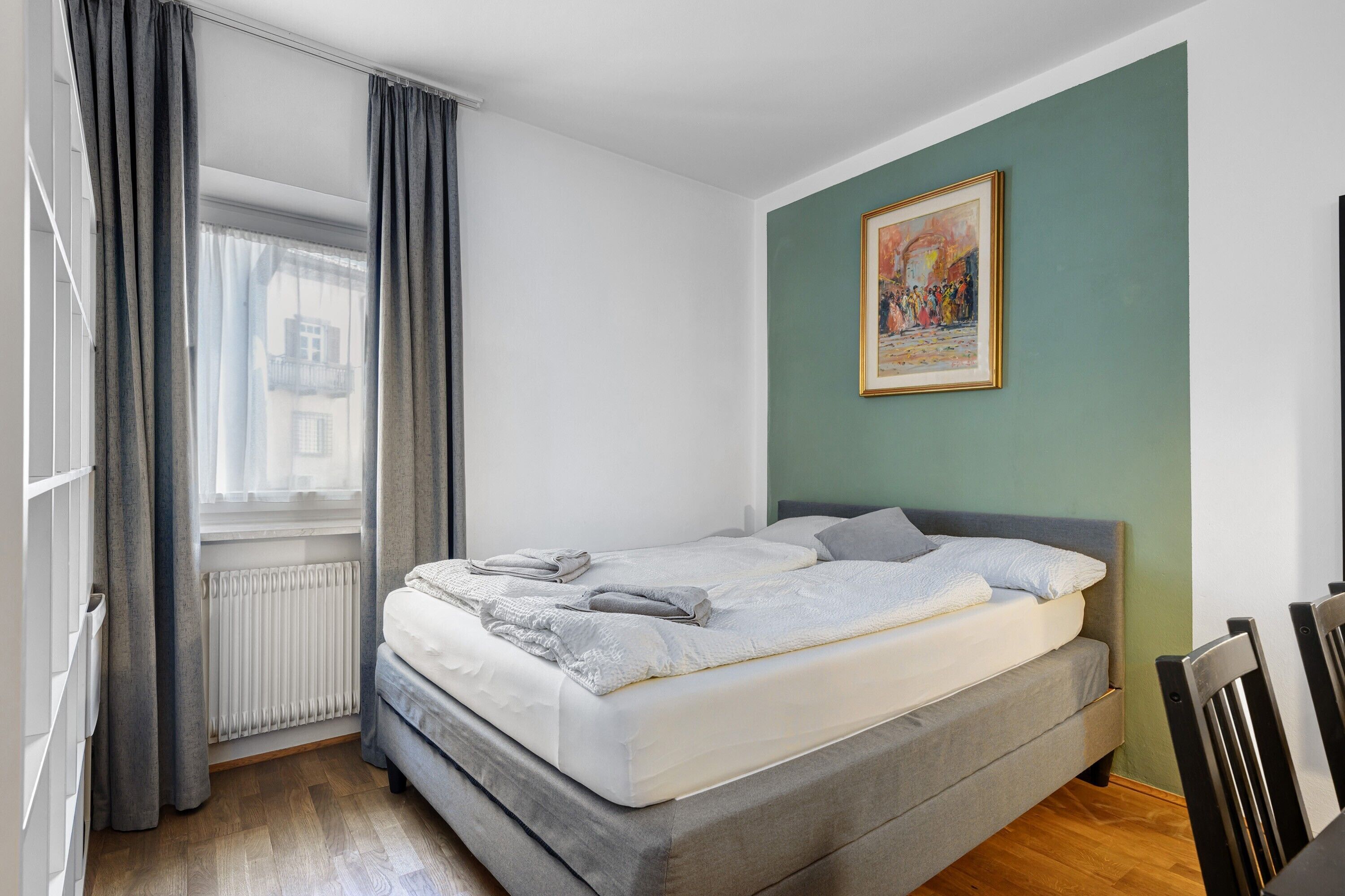 Ein Schlafzimmer mit einem Bett, einem Heizkörper, einem Fenster mit Vorhängen und einem Bild an der Wand.