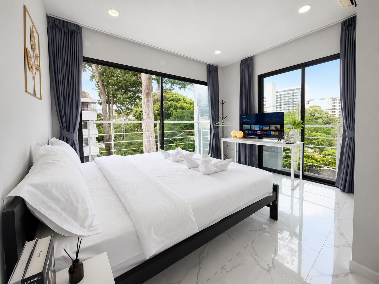 A modern hotel room with a large bed, a flat-screen TV, and a balcony with a city view.
