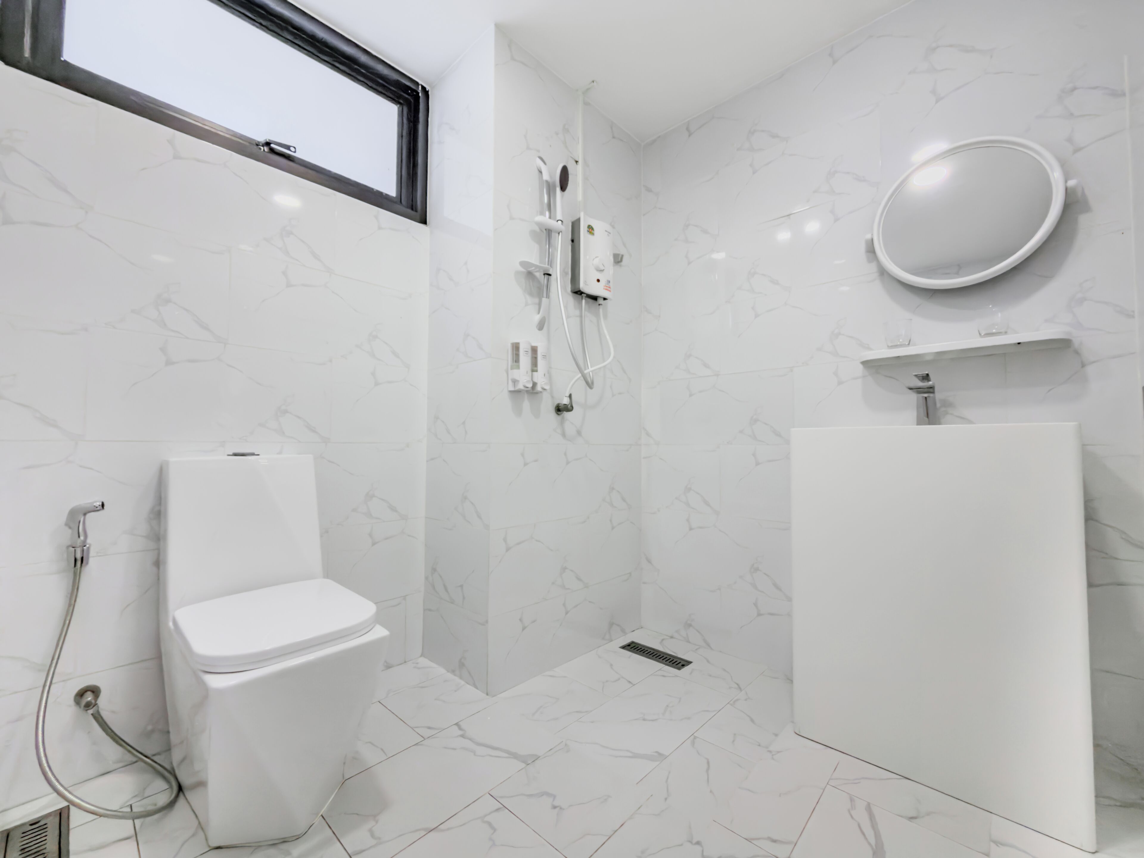 Un baño moderno con inodoro, ducha y lavamanos, todo en color blanco.