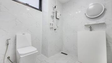 Un baño moderno con inodoro, ducha y lavamanos, todo en color blanco.