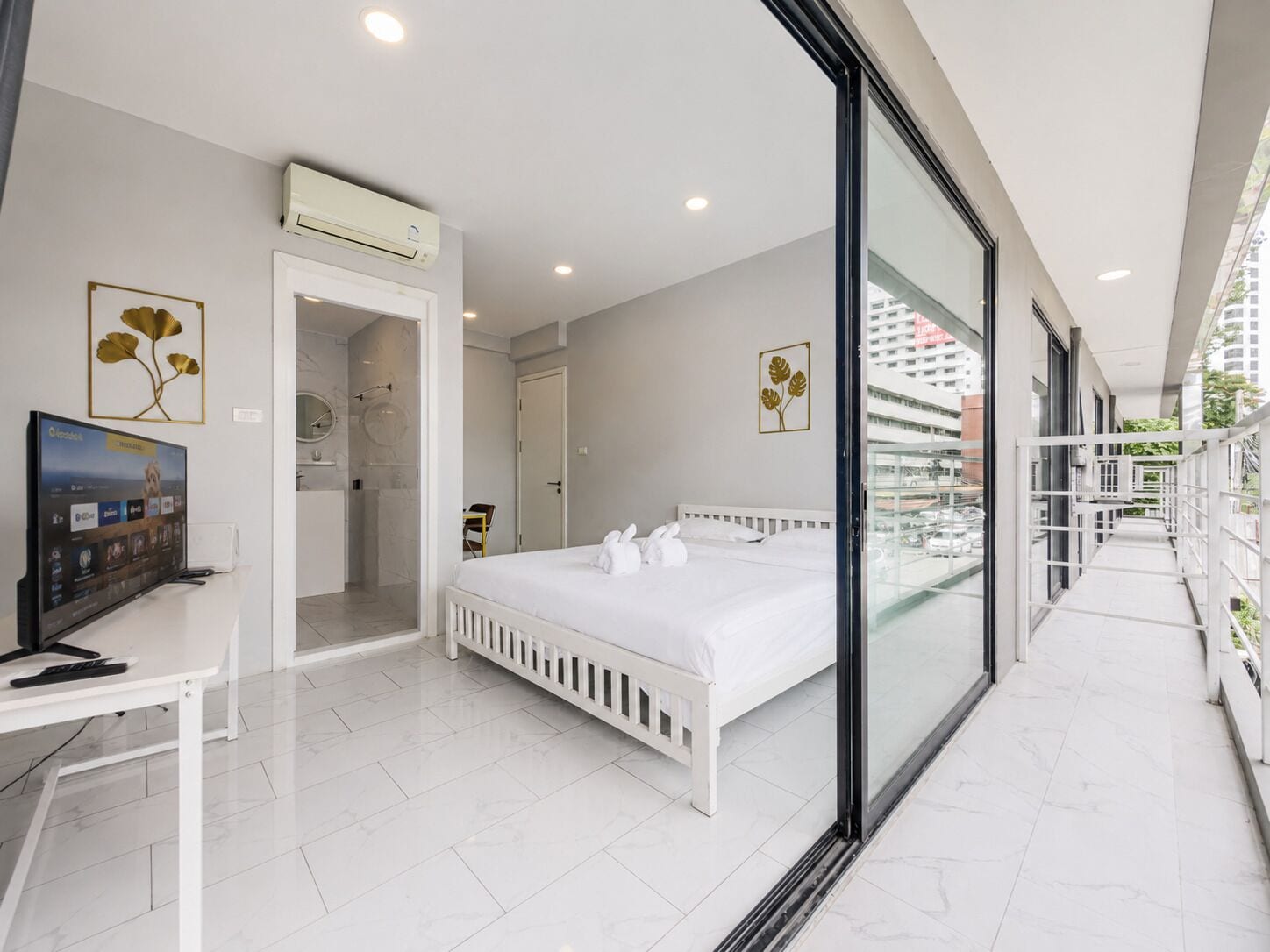 Ein modernes Hotelzimmer mit Bett, Schreibtisch mit Computer, Badezimmer und Balkon mit Blick auf die Stadt.