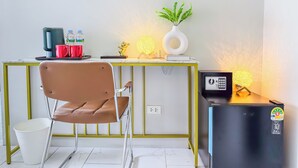 Een moderne kamer met een bureau, stoel, koffiezetapparaat, waterfles, decoratieve voorwerpen en een kleine koelkast.