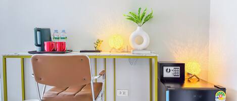 Une chambre moderne équipée d’un bureau, d’une chaise, d’une machine à café, d’une bouteille d’eau, d’objets de décoration et d’un petit réfrigérateur.