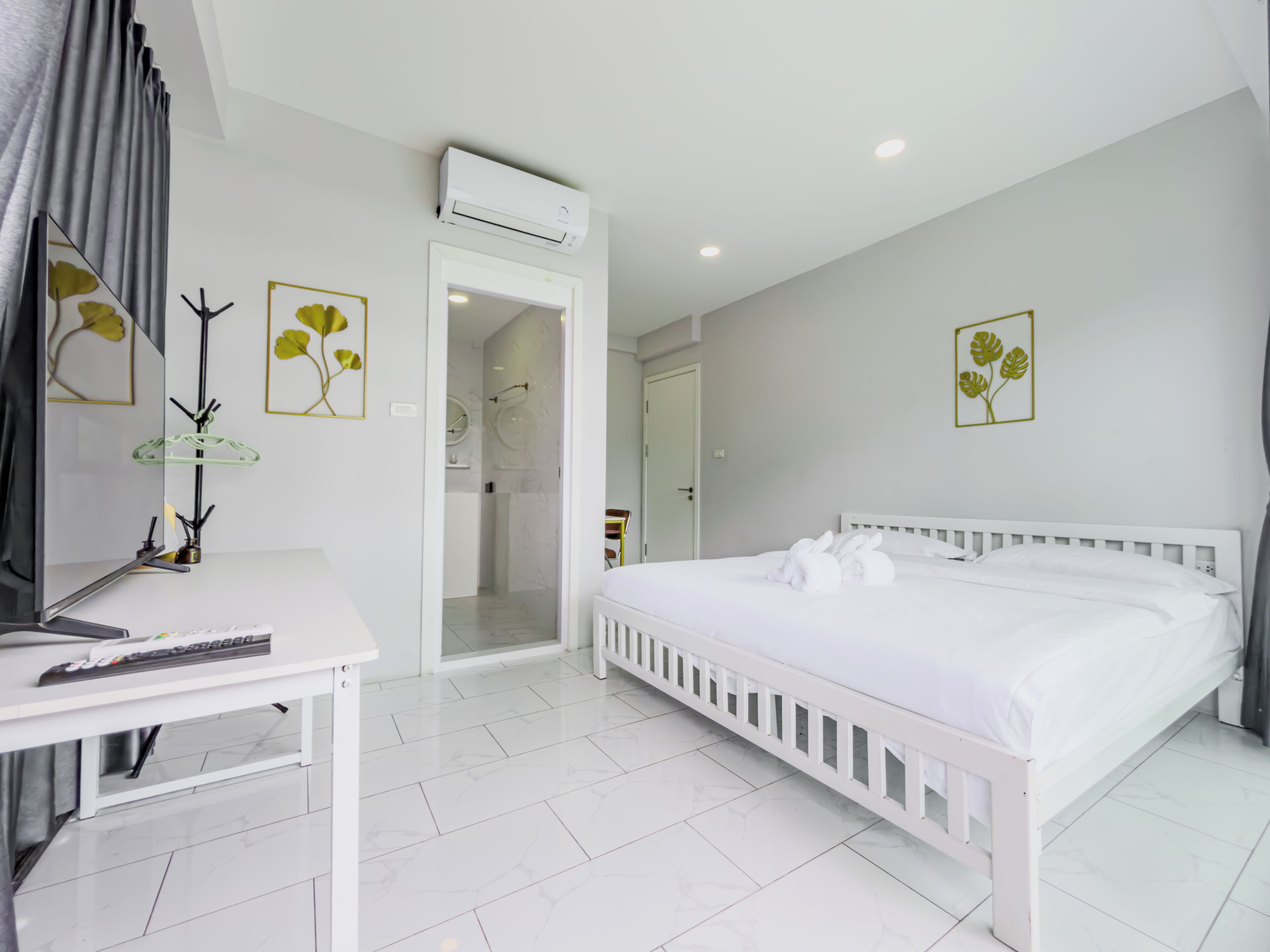A hotel room with a white bed, a desk with a keyboard, a mirror, and a door leading to a bathroom.