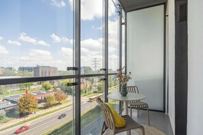 Un balcon donnant sur un paysage urbain, une table avec un vase et deux chaises.