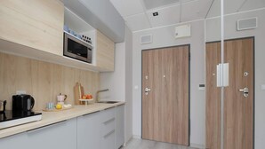 Una cucina moderna con forno a microonde, bollitore e ciotola di frutta. Si notano due porte in legno e un piano di lavoro bianco.