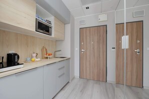 A modern kitchen with a microwave, kettle, and fruit bowl. There are two wooden doors and a white countertop. - Stylish Studio with a Balcony Central Warsaw (Warszawa)