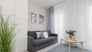 Un soggiorno moderno con un divano grigio, due opere d'arte incorniciate, un tavolino con fiori e un'ampia finestra con tende leggere.