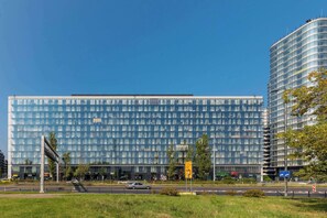 Un bâtiment moderne à la façade en verre, situé près d’une route où se trouve un passage piéton.