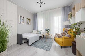 A modern, well-lit room with a bed, a yellow armchair, a small table with a vase of flowers, and a potted plant. - Stylish Studio with Balcony | Warsaw Center (Warszawa)
