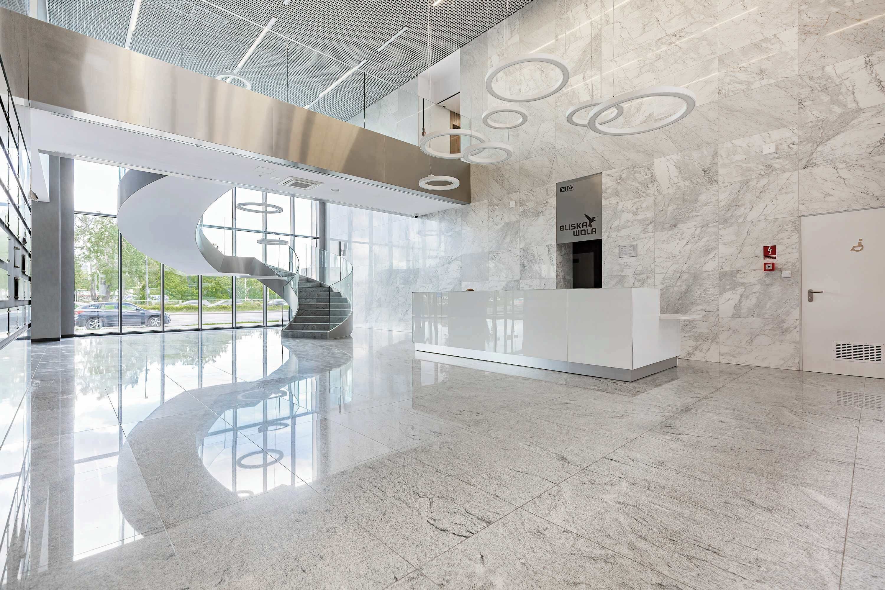 A modern lobby with a marble floor, a spiral staircase, and a reception desk.