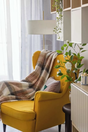 A yellow armchair with a plaid throw blanket, a white radiator, and a plant with white flowers. - Stylish Studio with a Balcony Central Warsaw (Warszawa)