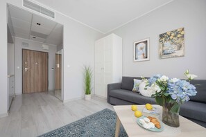 A modern living room with a grey sofa, a coffee table with a vase of flowers, and a painting on the wall. - Stylish Studio with Balcony | Warsaw Center (Warszawa)