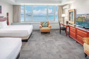 Ein Hotelzimmer mit zwei Betten, einem Sessel, einem Fernseher und Meerblick.