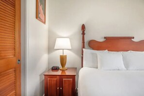 Ein Hotelzimmer mit Holztür, Nachttisch mit Lampe und einem Bett mit weißer Bettwäsche.