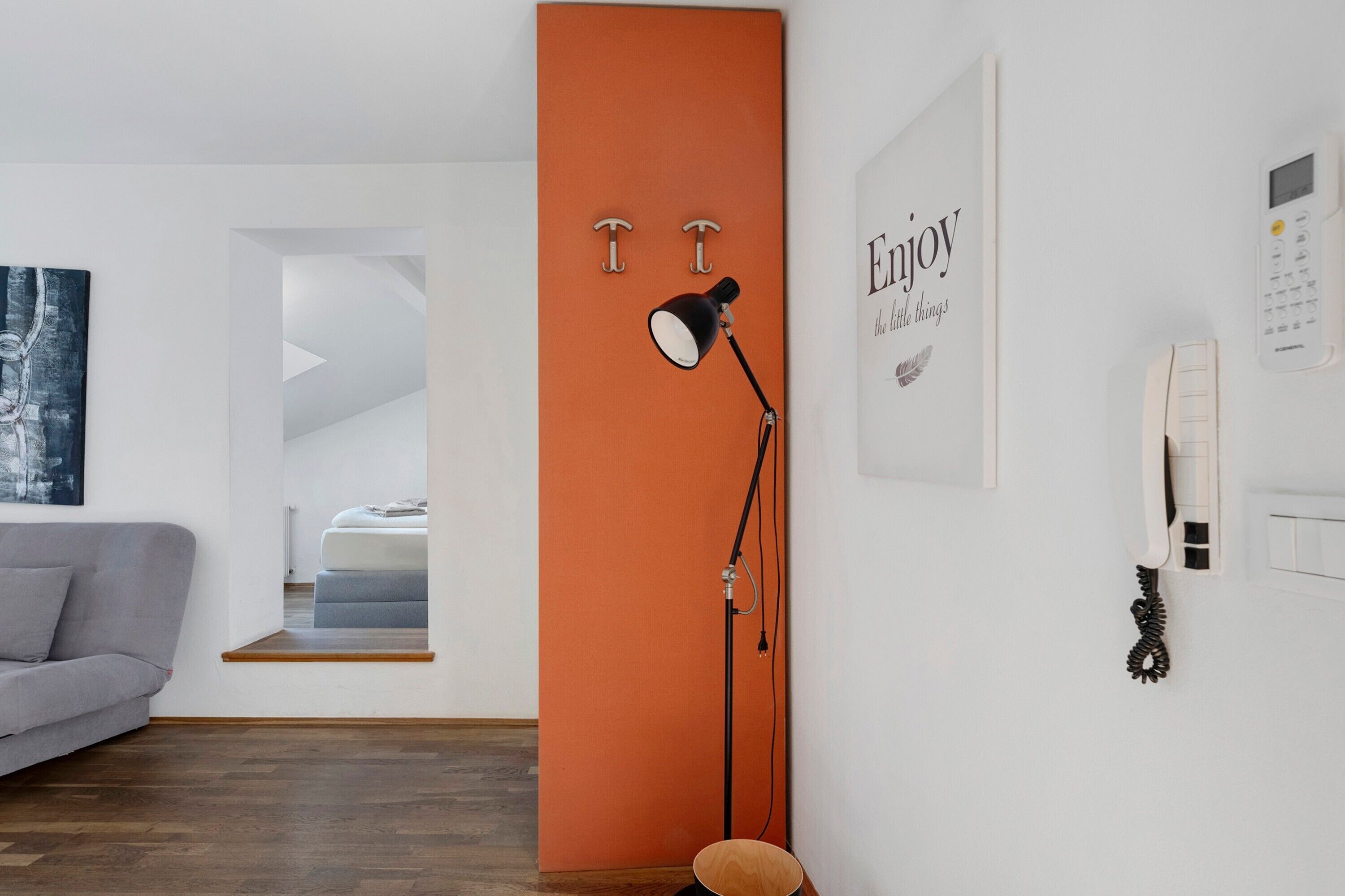 Ein modernes Wohnzimmer mit grauem Sofa, Holzboden, einer orangefarbenen Akzentwand, einer schwarzen Stehlampe und einem gerahmten Motivationszitat.