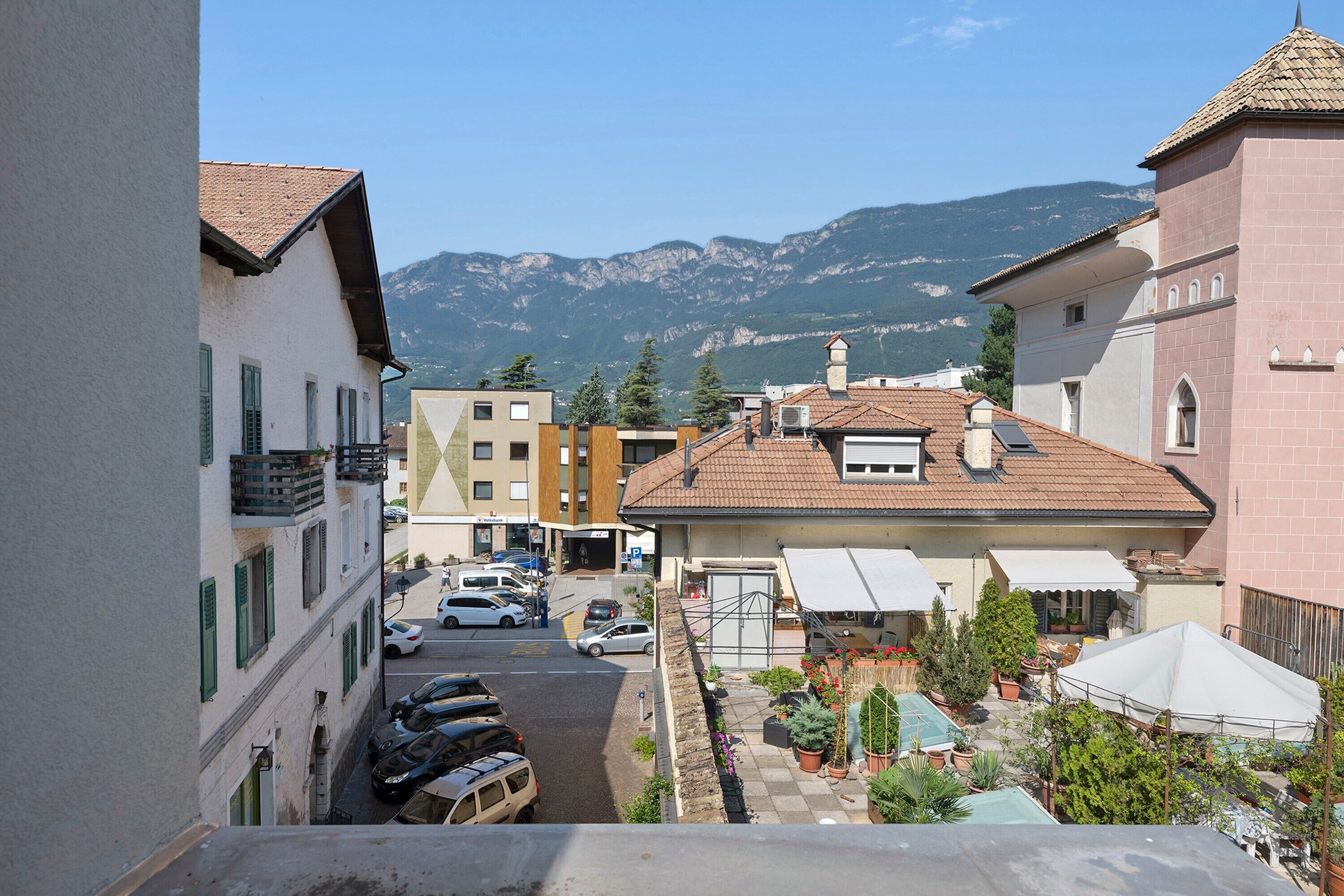 Eine Wohnstraße mit parkenden Autos, ein Gebäude mit Satteldach und Berge im Hintergrund.