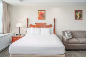 Ein Hotelzimmer mit einem großen Bett, einem hölzernen Kopfteil, einem Nachttisch mit Lampe, einem beigen Sofa und zwei gerahmten Bildern an der Wand.