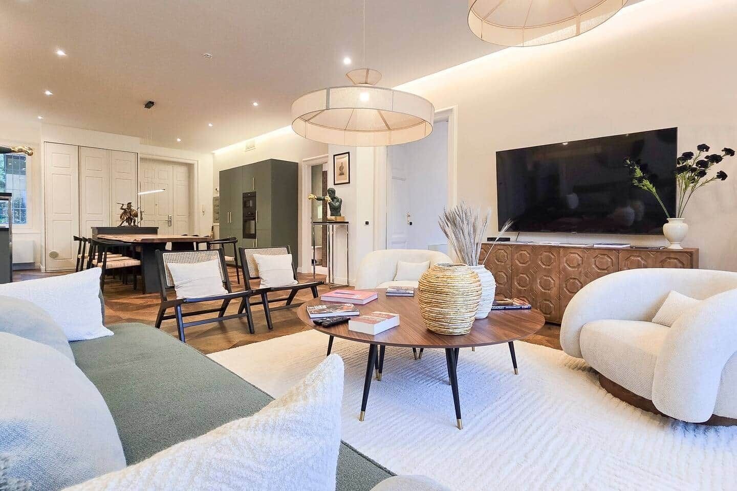 Ein modernes Wohnzimmer mit einer Couch, Sesseln, einem Couchtisch und einem Fernseher.