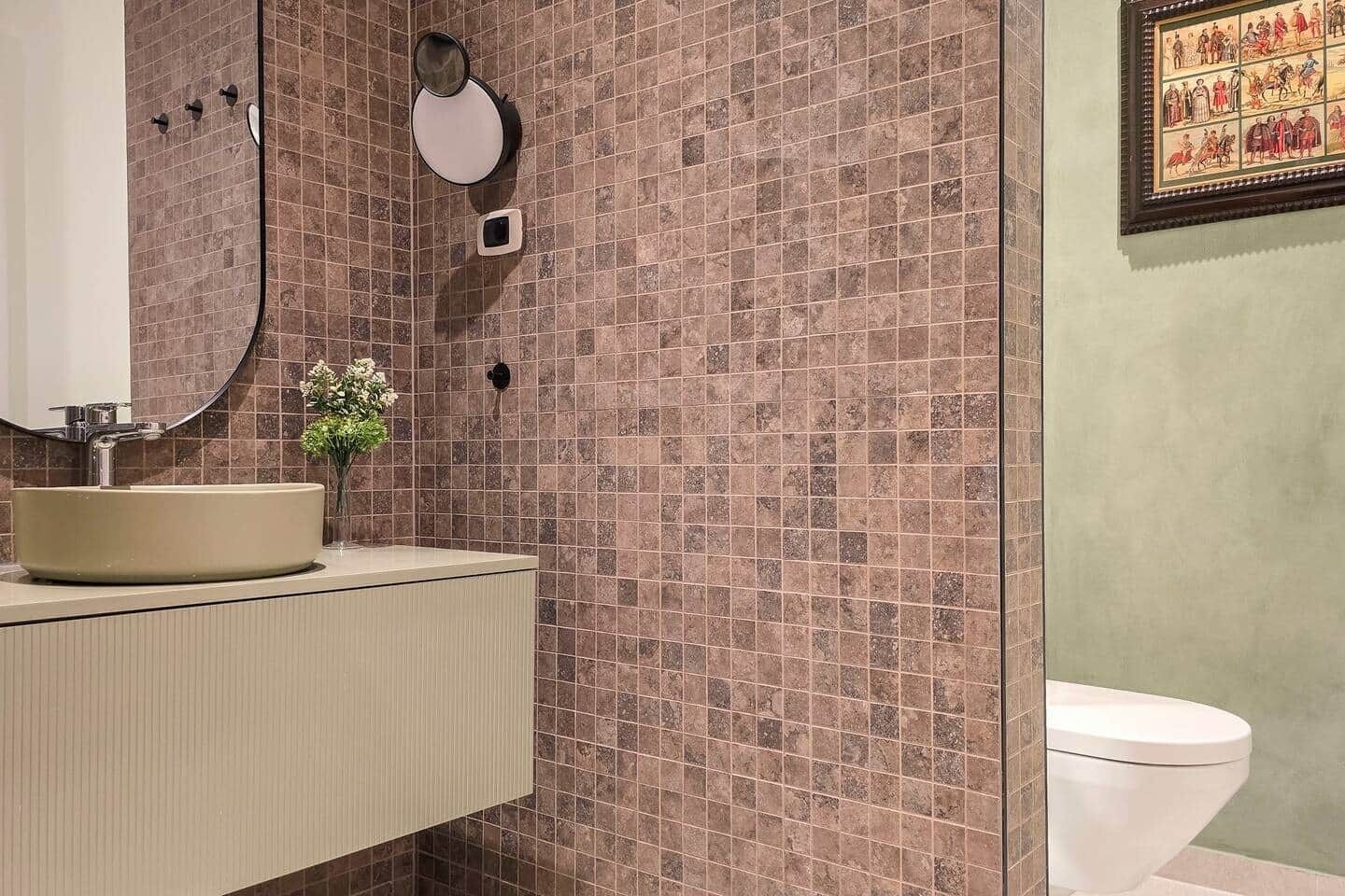 A bathroom with a round sink, a mirror, a small plant, and a toilet.