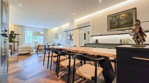 Une cuisine moderne avec une longue table en bois, des chaises noires et une statue posée sur le comptoir.