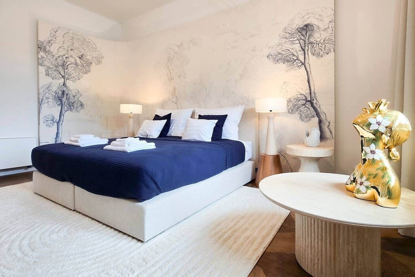 A modern hotel room with a large bed, bedside lamps, a round table, and a decorative golden animal figurine.