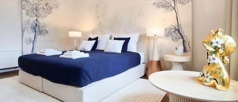 A modern hotel room with a large bed, bedside lamps, a round table, and a decorative golden animal figurine.