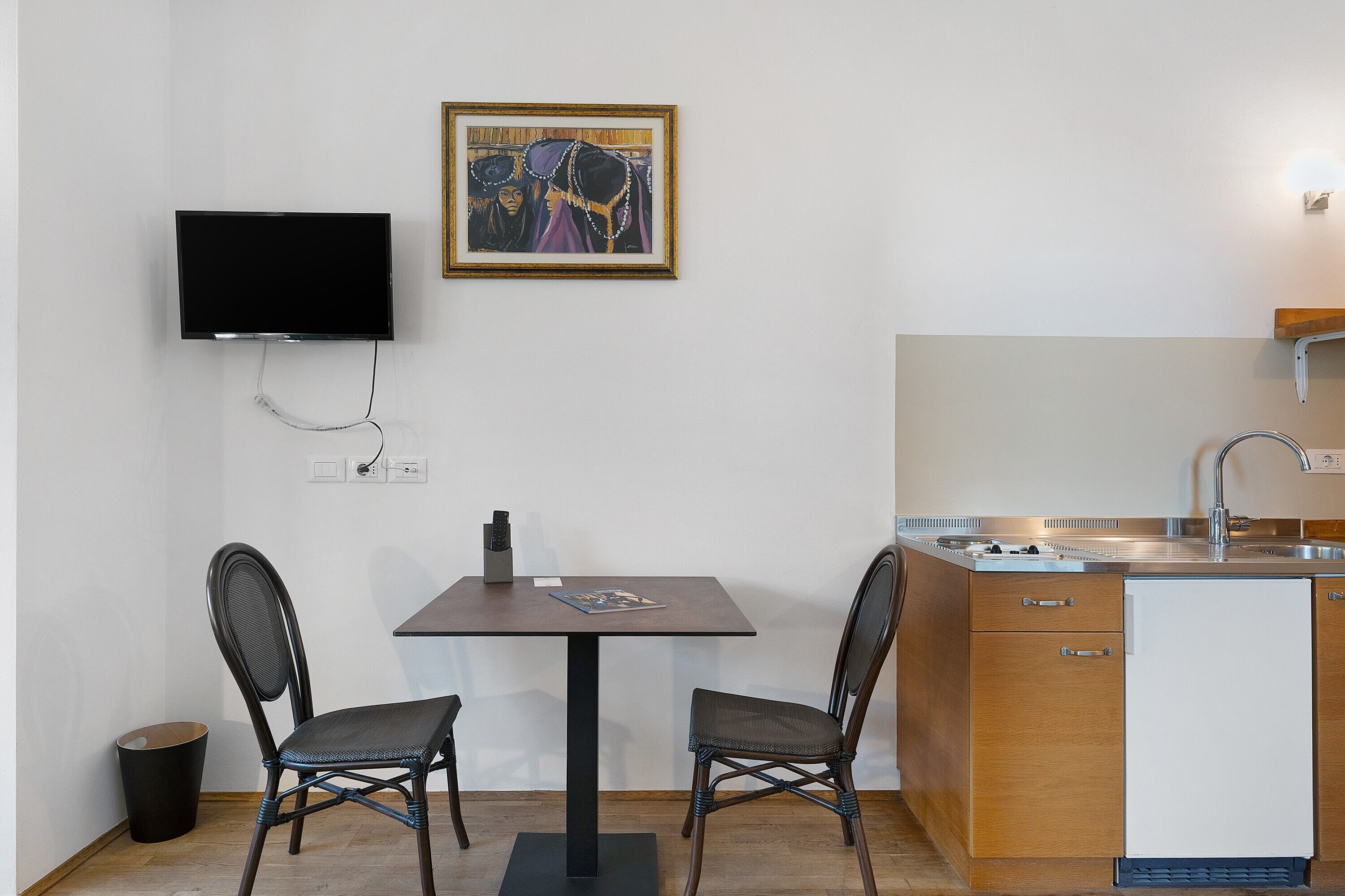 Une petite cuisine équipée comprenant une petite table et des chaises, un téléviseur fixé au mur et une seule poubelle.