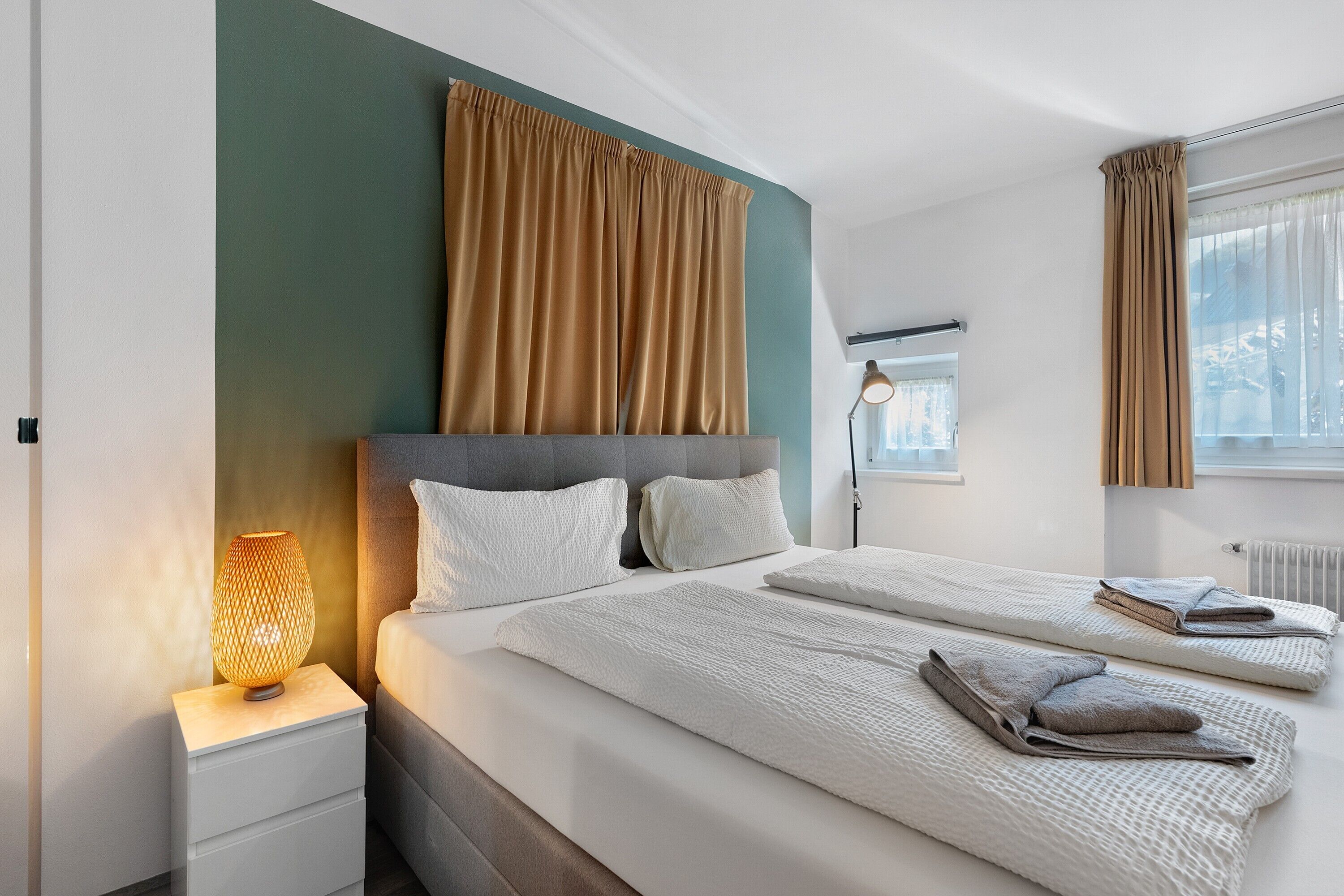 Una habitación de hotel con cama, mesitas de noche, lámpara y cortinas.
