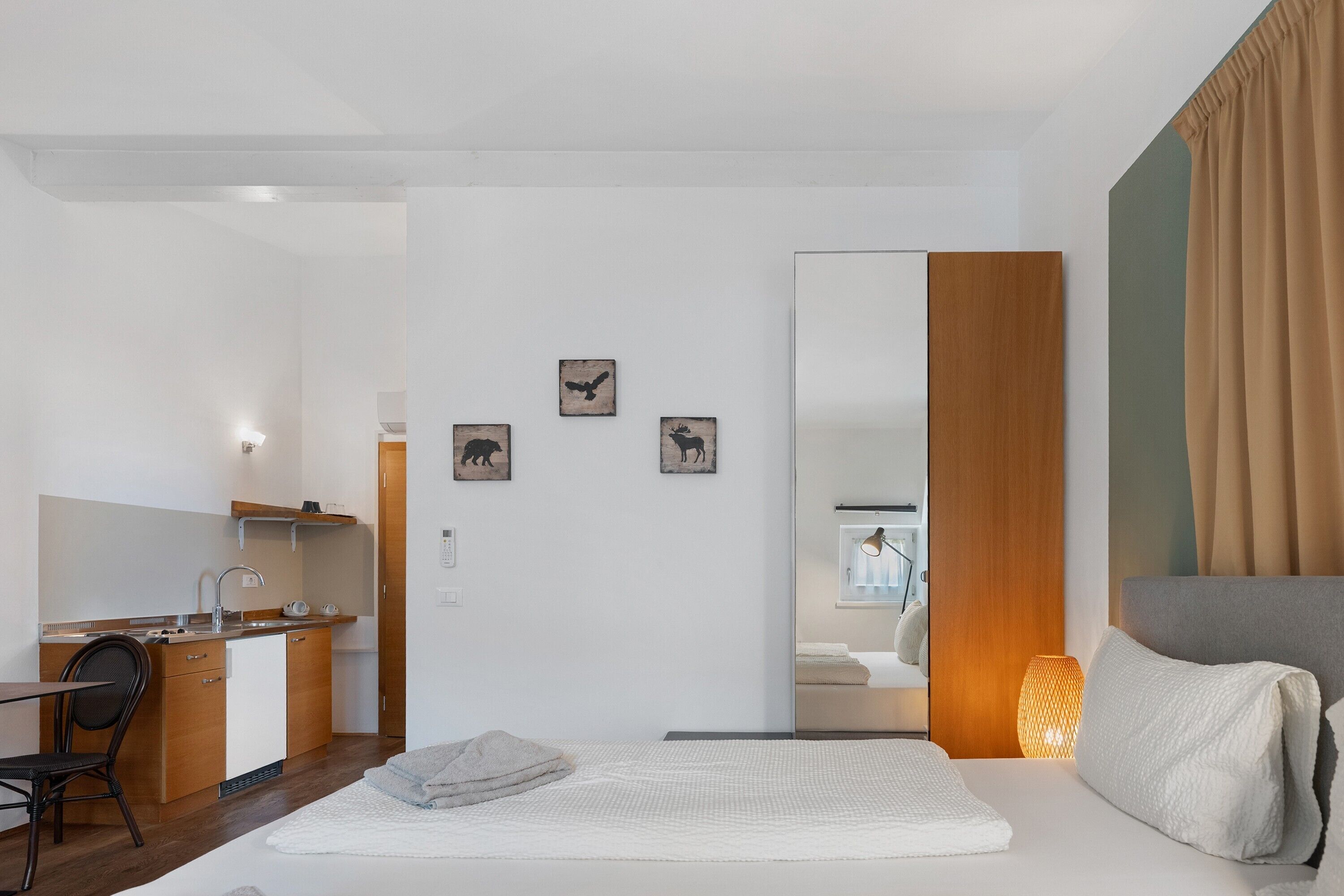 Ein kleines Hotelzimmer mit einem Bett, einem Schreibtisch mit Stuhl, einer kleinen Küchenzeile und einem Badezimmer.
