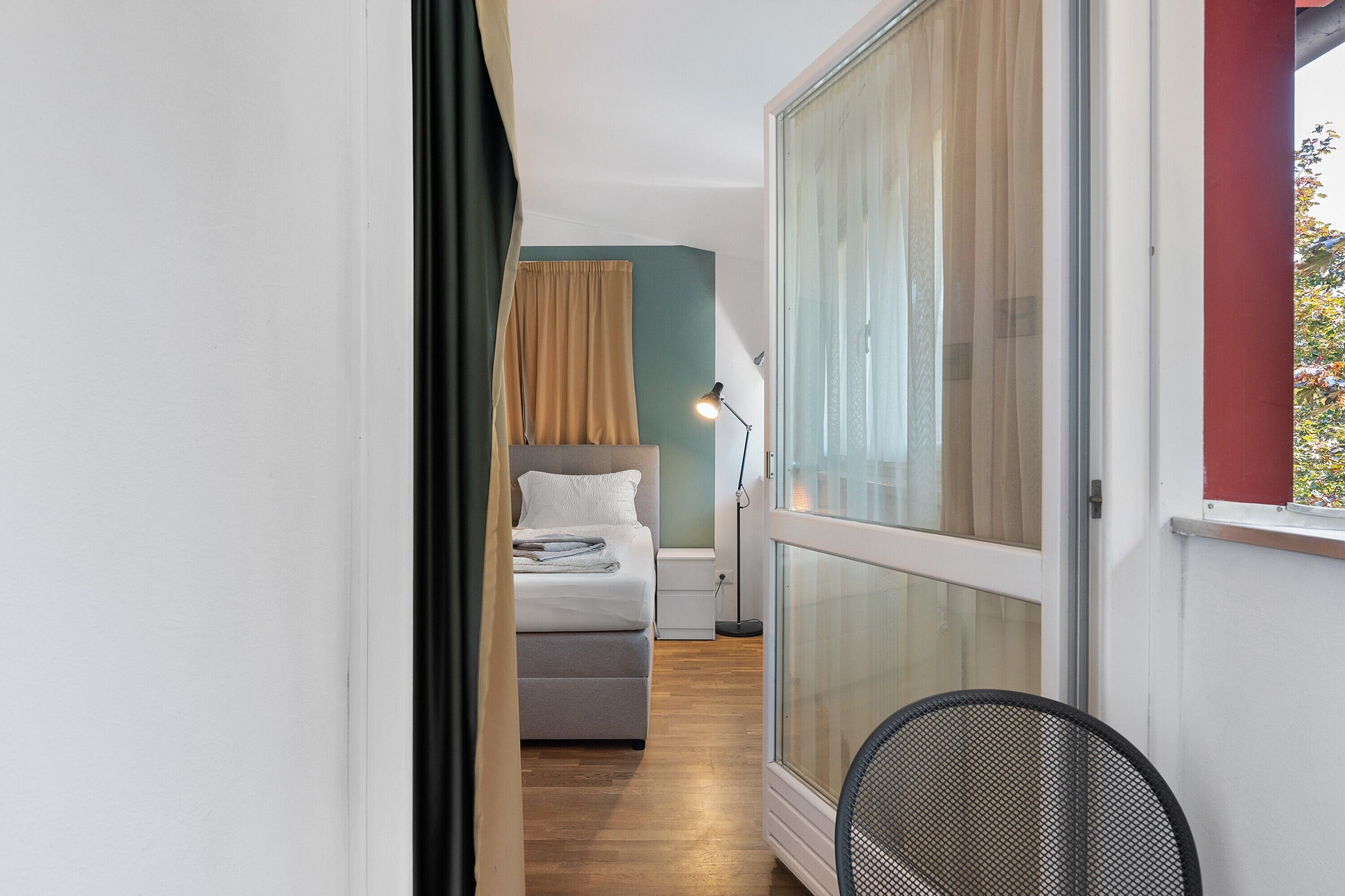 A narrow hallway leading to a bedroom with a bed, a desk, and a chair.