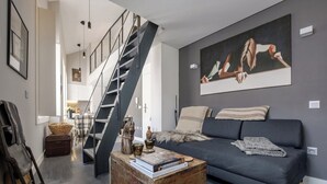 Uma sala de estar moderna com um sofá cinza escuro, uma mesa de centro de madeira e uma escada que leva a um andar superior.