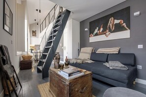 Ein modernes Wohnzimmer mit einem dunkelgrauen Sofa, einem Holztisch und einer Treppe, die zu einer oberen Ebene führt.