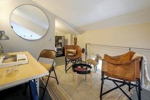 Ein Zimmer mit einem runden Spiegel, einem Holztisch mit einer Lampe, zwei Ledersesseln, einem kleinen runden Tisch und einer Whiteboard-Tafel.