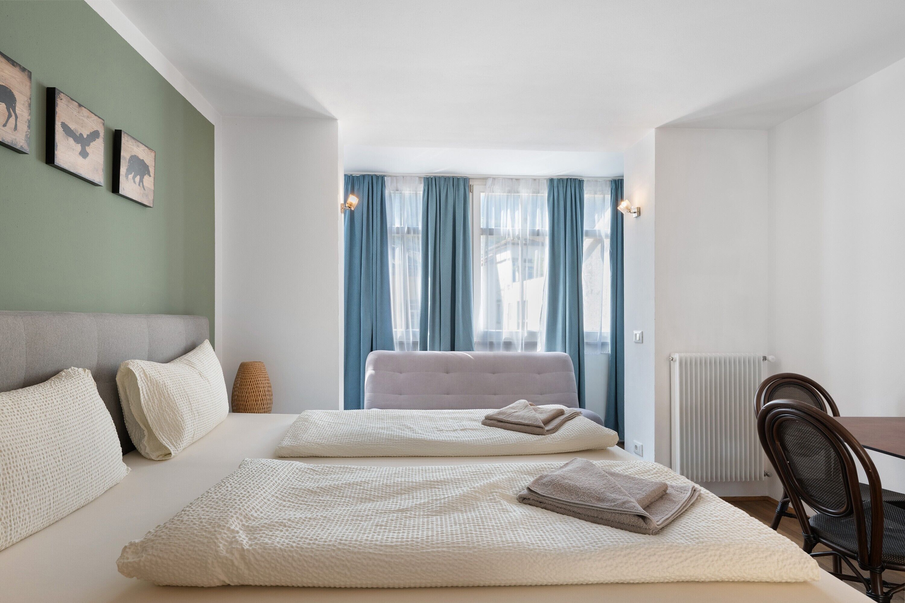 Habitación de hotel con cama, dos almohadas, una silla, una mesa y ventana con cortinas.