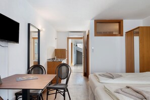Habitació d'hotel amb un llit, escriptori i cadires, televisió i bany visible a través d'una porta oberta.