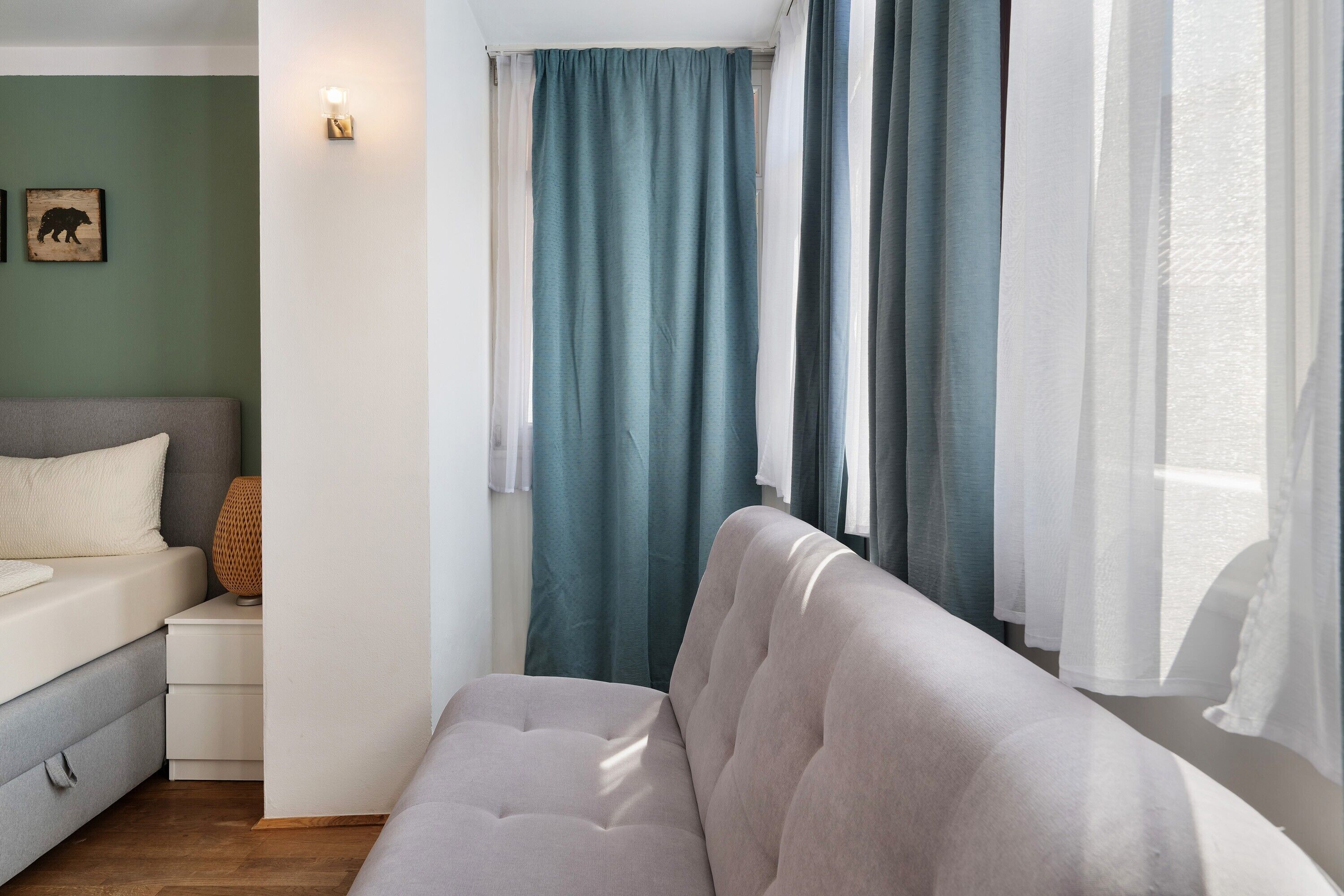Ein modernes Schlafzimmer mit einem grauen Sofa, einem kleinen Nachttisch, einer Lampe und einer grünen Wand.