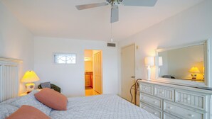 Ein Schlafzimmer mit Bett, Nachttischlampen, einem Schminktisch, einem Spiegel und einem Deckenventilator.