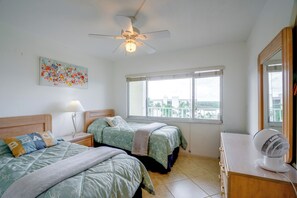 A bedroom with two beds, a ceiling fan, a window with a view, and a bedside table with a lamp. - On the Beach Condo for the Ultimate in Relaxation (Bonita Springs)
