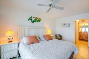 A bedroom with a bed, two bedside lamps, a ceiling fan, and a wall-mounted decorative piece. - On the Beach Condo for the Ultimate in Relaxation (Bonita Springs)