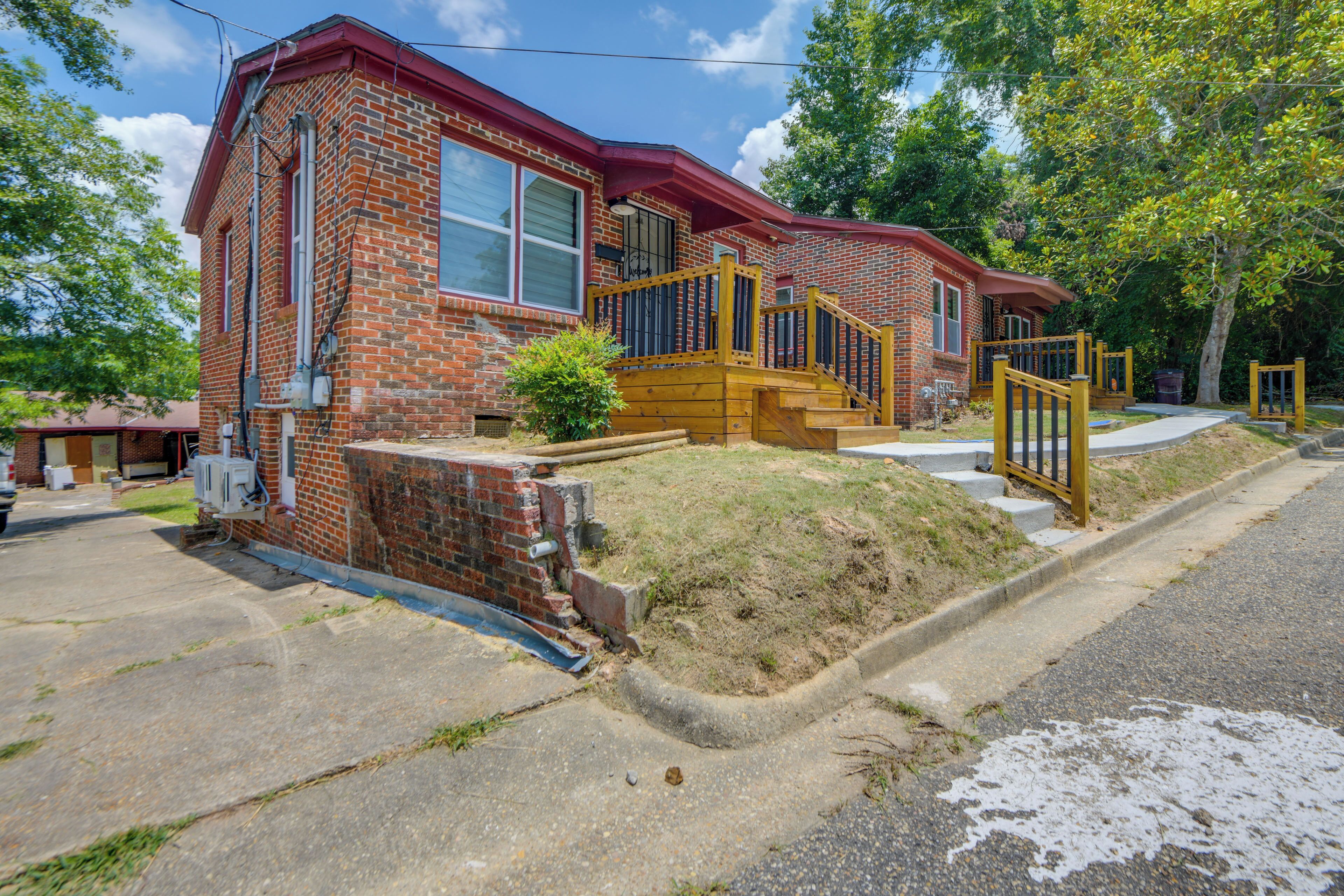 A two-story brick house with a red roof, a front porch, and a wooden staircase leading to the entrance.