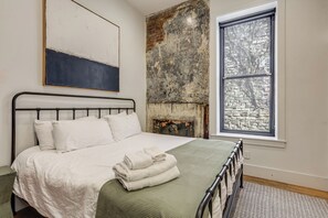 Ein Schlafzimmer mit einem Bett, einem Fenster, einer Ziegelwand und einem Gemälde.